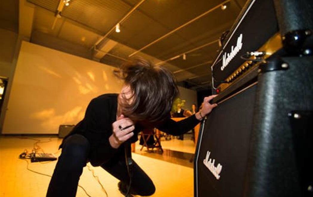 A person headbanging is singing into a microphone squatting down, holding onto the speaker